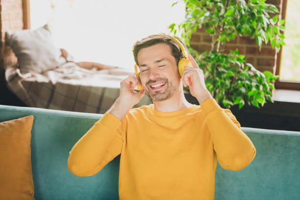 漂亮的年轻人的照片肖像耳机听音乐坐在沙发上穿黄色的衣服现代室内平坦的室内图片下载