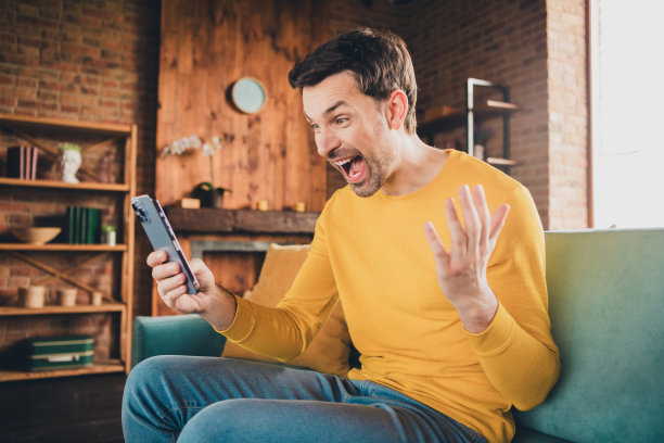 漂亮年轻人的照片肖像激动地拿着设备新闻坐在沙发上穿着黄色的衣服现代室内平坦的室内图片下载