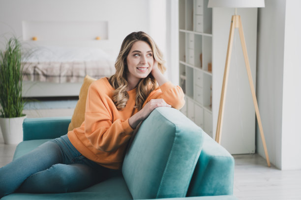 迷人的年轻女子的照片肖像坐在沙发上看起来梦幻的窗户穿着橙色的衣服舒适的日光家室内客厅图片下载