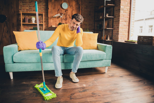 漂亮年轻人的全身照片拖地打扫房子坐沙发沮丧疲倦穿黄色衣服现代室内平坦的室内图片下载