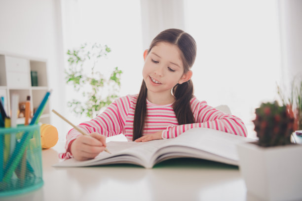 年轻的黑发女学生的照片，她待在家里准备考试，在笔记本上写笔记，独自坐在书桌上度假图片下载
