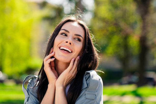 美丽的年轻微笑西班牙迷人的女士穿着灰色大衣城镇当地公园触摸脸颊放松在自然的肖像照片图片下载