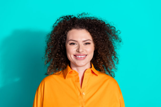 照片的好心情积极开朗的女人波浪发型，穿着橙色t恤微笑孤立的绿松石色背景图片下载