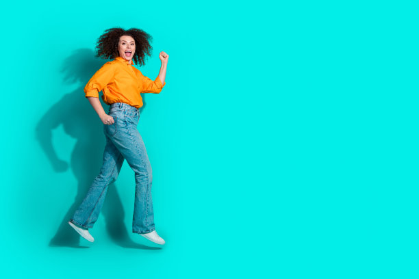 一个穿着橙色衬衫牛仔裤的时髦乐观的女人的全尺寸照片，在蓝绿色背景的空白空间里出售图片下载