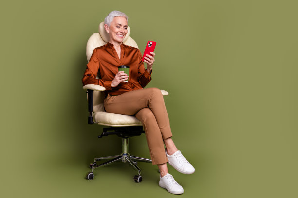 退休女性的全尺寸照片坐在办公室扶手椅喝咖啡装置穿棕色正装孤立在卡其色背景图片下载