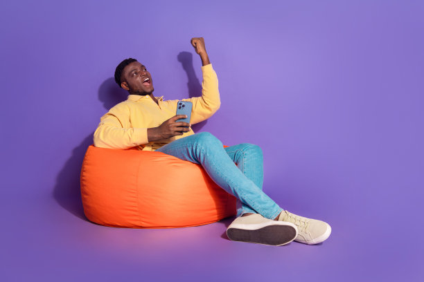 英俊的年轻人的全身照片坐在豆袋赢得小玩意穿着时尚的黄色服装孤立在紫色的背景图片下载