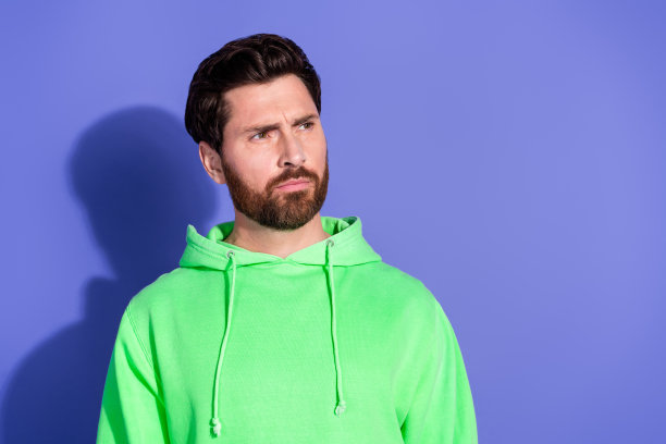 照片的英俊成熟的男子困惑和穿着明亮的霓虹卫衣看起来copyspace可疑孤立在紫罗兰色的背景图片下载