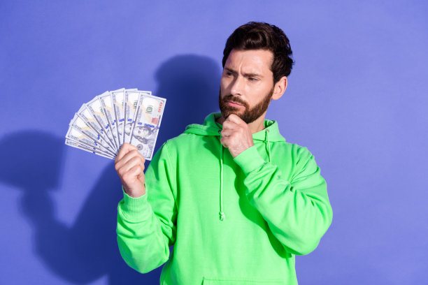 照片中英俊的年轻人抱着看起来很有头脑的钱迷，穿着时尚的绿色服装，孤立在紫罗兰色的背景上图片下载