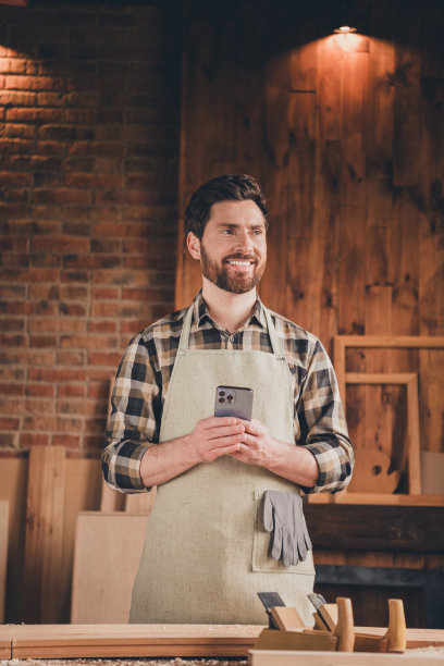 小伙工匠站在车库车间的照片，站着看，拿着使用手机智能小工具图片下载