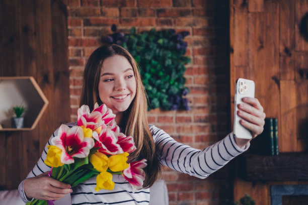 照片迷人的少女手持鲜花花束郁金香自拍照片穿着条纹装昼光家室内客厅图片下载