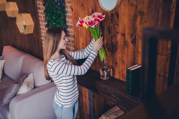 漂亮的年轻女孩的照片放鲜花花瓶穿条纹套头衫阁楼室内公寓室内图片下载