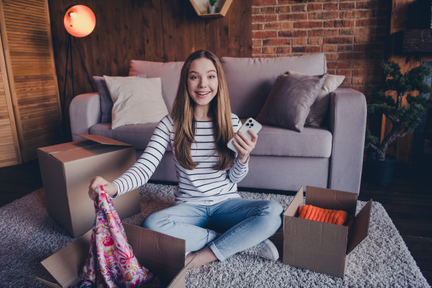 可爱的年轻女孩的全尺寸照片拿着手机打开盒子穿套头衫现代阁楼室内公寓室内图片下载