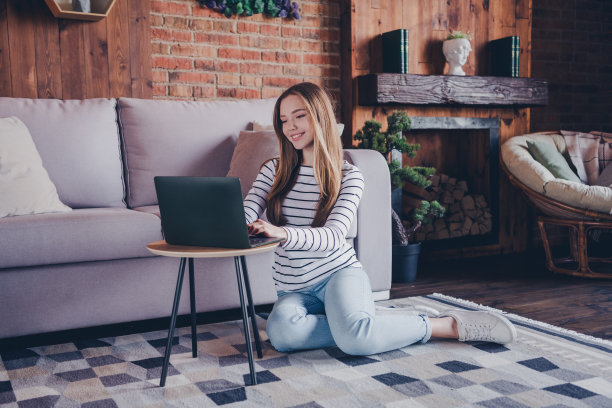 可爱少女的全身照片坐在地板上网本放松穿着条纹服装花消遣宽敞的房子室内房间图片下载