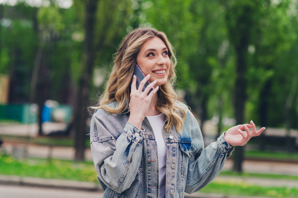 漂亮的年轻女子的照片讲电话穿牛仔夹克自由时间散步新鲜空气公园户外图片下载