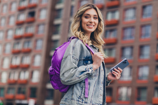 漂亮的年轻女子的个人资料照片拿着手机背包，穿着牛仔夹克走在市中心户外图片下载