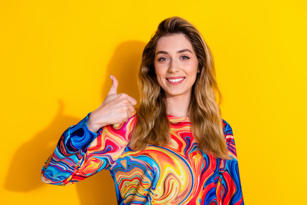 照片中的年轻有趣的金发女子穿着彩色套头衫享受这个服务拇指向上的手势孤立的黄色背景图片下载