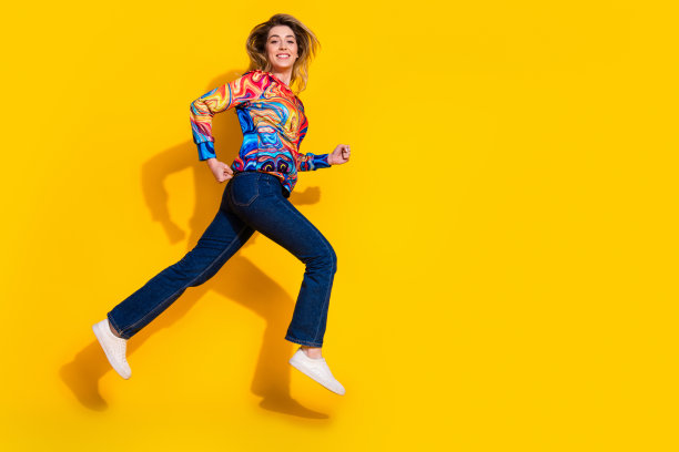 照片肖像的积极运动跑步妇女穿着彩色套头衫和牛仔裤测试她的新鞋孤立的黄色背景图片下载