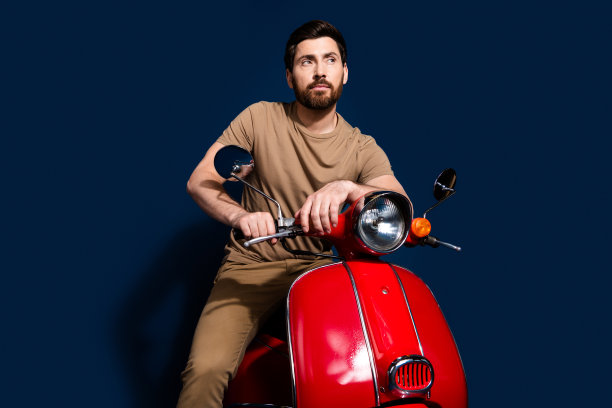 照片中快乐的年轻人穿着米色t恤喜欢夏天骑摩托车沉思看着道路孤立的深蓝色背景图片下载