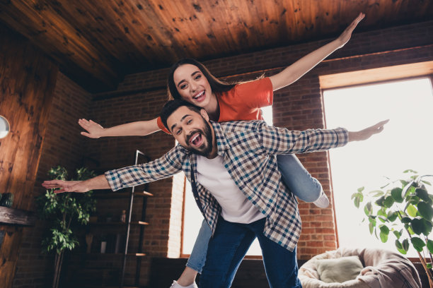 欢快可爱的年轻夫妇的照片背在背上摊开手玩得开心享受周末玩得开心买新公寓在室内在家里图片下载