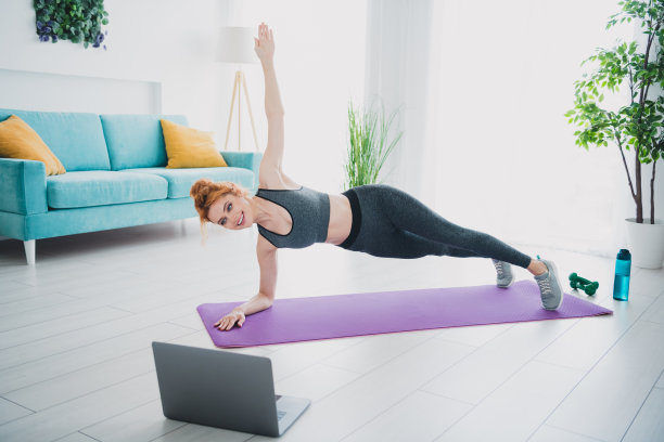 照片的运动漂亮的女人穿着运动服观看视频课平板支撑练习白天在室内图片下载