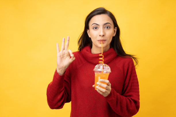 年轻女子的肖像喝冷饮穿针织套头衫孤立的黄色背景股票照片图片下载