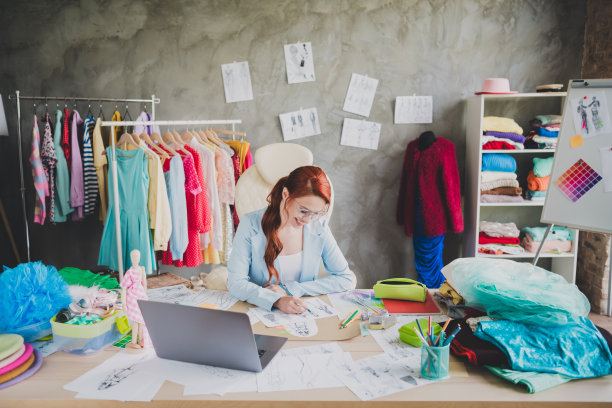 创意女孩时装设计师在工作室商店商店坐在桌子上画纸草图衣服的照片图片下载