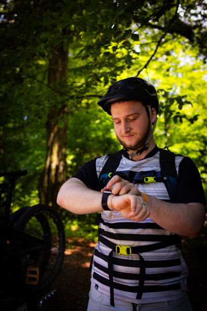 年轻的山地自行车手戴着头盔检查智能手表。垂直的照片。图片下载