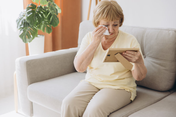 沮丧的老年妇女抱着相框，看着家里家人的旧照片，伤心的老人哭泣，对着丈夫和儿子的旧照片呻吟，想念爱人，孤独图片下载