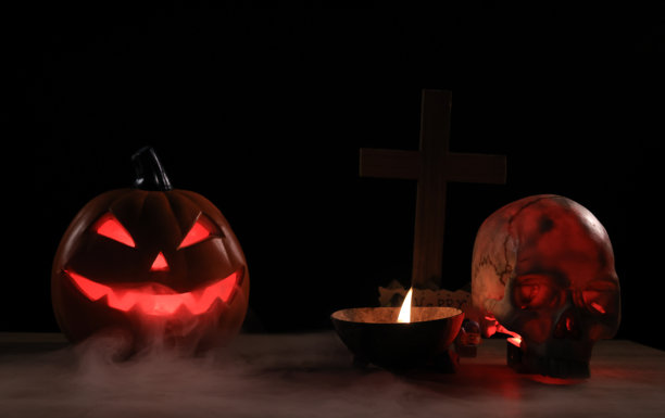万圣节南瓜与蜡烛，烟，和一个人的头骨在黑色的背景。可怕的万圣节标志图片下载