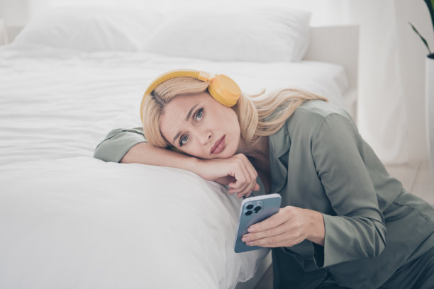 漂亮的年轻女子的照片耳机电话哭泣丝绸睡衣白色室内卧室公寓室内图片下载