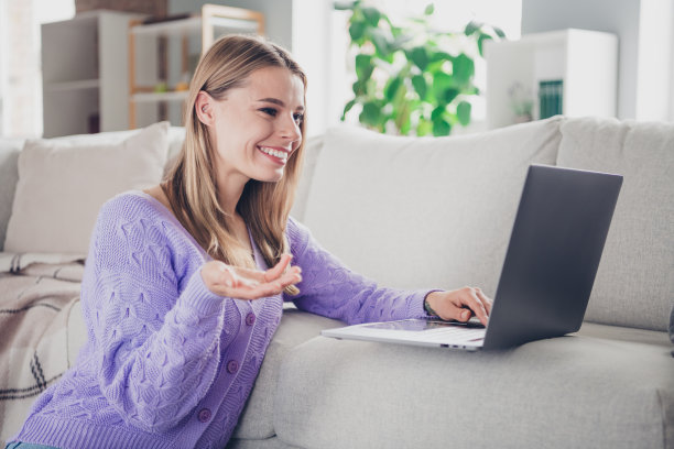 可爱开朗的女孩照片坐在地板沙发上网本视频通话穿着紫色的衣服度过休闲宽敞的房子室内房间图片下载