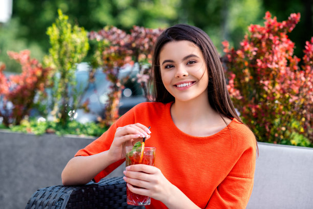 照片漂亮的青少年好心情的女孩坐在早餐喝鸡尾酒穿着红色的衣服走在城市公园外图片下载
