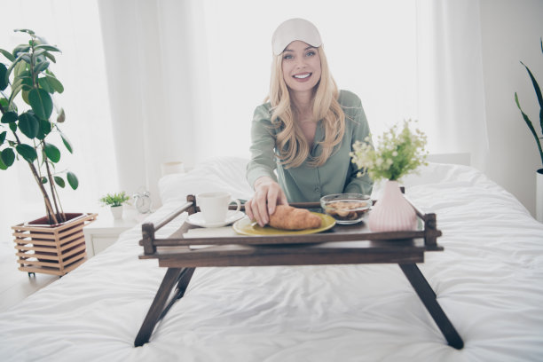 漂亮年轻女子的全尺寸照片早餐床羊角面包咖啡睡衣白色室内卧室公寓室内图片下载