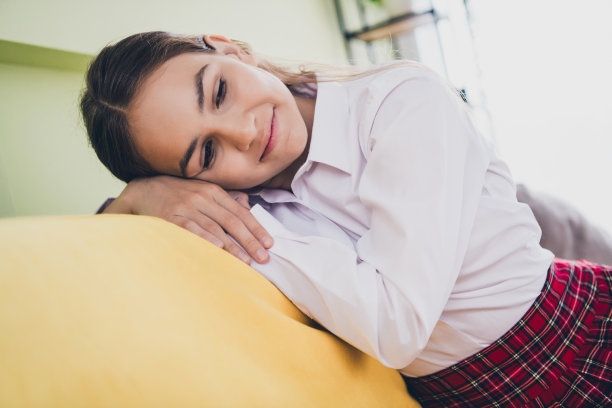 可爱的十几岁的女学生的照片肖像梦幻的坐沙发放松享受舒适穿校服家教育概念学校内部图片下载
