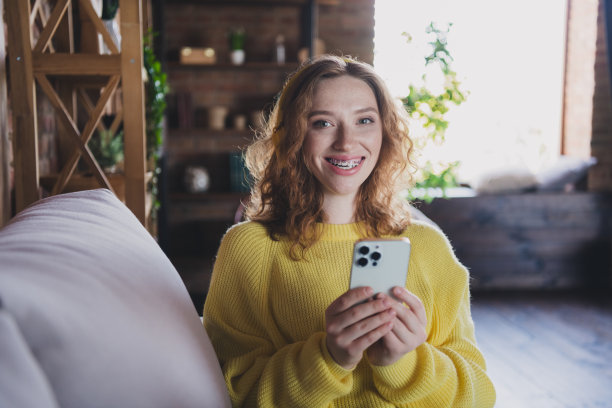 迷人的年轻女性坐在沙发上抱着装置穿着黄色毛衣舒适的日光家庭室内客厅的照片图片下载