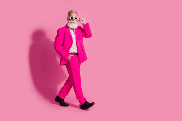 严肃的老酷男人绅士男友走路的全身照片，戴着太阳镜，时尚的粉红色西装孤立在柔和的颜色背景图片下载