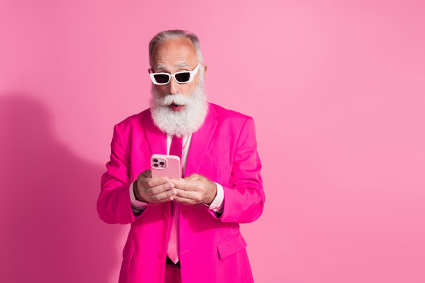 照片中严肃的老酷男人绅士男友惊讶地拿着装置戴着太阳镜时髦的粉色西装孤立在柔和的颜色背景图片下载