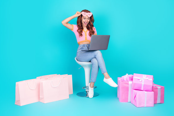 漂亮的年轻女孩的全尺寸照片，坐在椅子上，现在购物上网本，穿着时髦的粉红色服装，孤立在海蓝宝石的背景图片下载