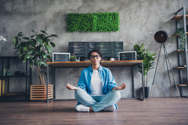 迷人的年轻女子全身照片坐在地板冥想穿蓝色衬衫现代办公室程序员阁楼房间室内室内工作空间图片下载