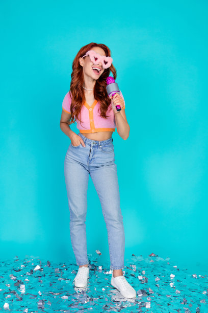 垂直的全尺寸照片漂亮的年轻女孩蓬松的太阳镜唱麦克风五彩纸屑穿时髦的粉红色服装孤立的海蓝宝石背景图片下载