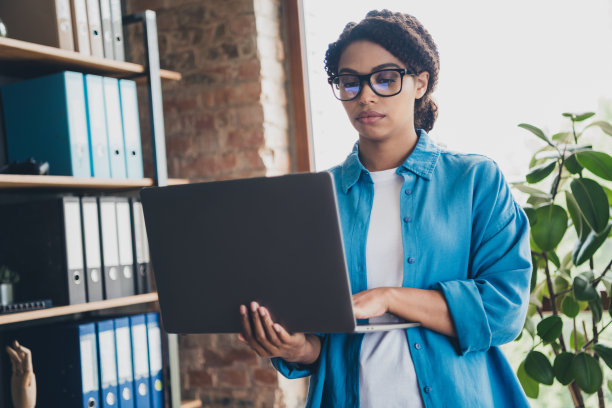 照片迷人的年轻女子拿着上网本穿蓝色衬衫现代办公室程序员阁楼房间室内室内工作空间图片下载