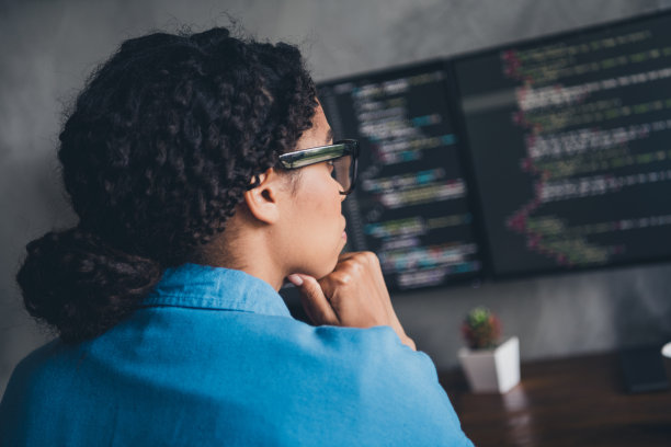 迷人的年轻女子编码的照片看显示器的头脑穿蓝色衬衫现代办公室程序员阁楼房间室内室内工作空间图片下载