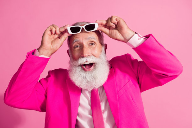迷人的白发老人的照片圣诞老人mc演出者脱下太阳镜，穿着时尚的粉红色西装孤立在柔和的颜色背景图片下载