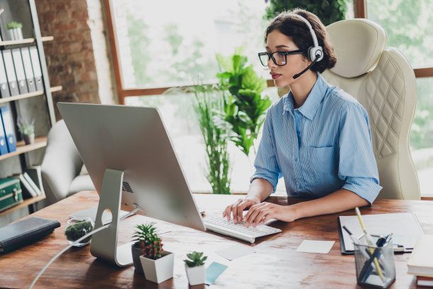 甜美迷人的女士助理的照片穿衬衫，眼镜，耳机短信现代设备在室内工作场所工作站图片下载