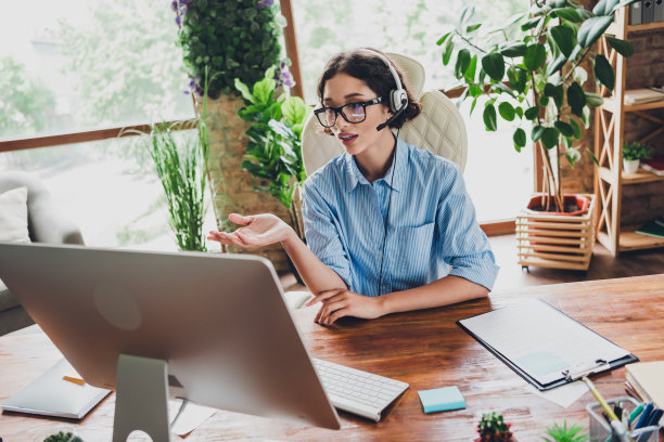 照片的甜美迷人的女士助理穿衬衫，眼镜，耳机说话的现代设备在室内工作场所工作站图片下载