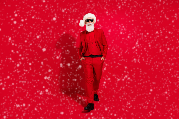 照片中自信帅气的圣诞老人双手口袋戴太阳镜圣诞帽西装鞋红色背景图片下载
