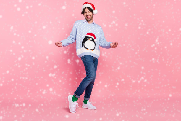 照片中迷人英俊的年轻人穿着蓝色圣诞套头衫，微笑着跳舞，孤立的粉红色背景图片下载