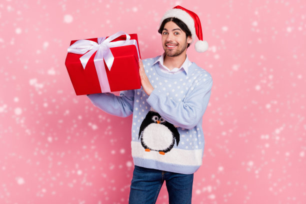 照片漂亮迷人的绅士穿着新年毛衣微笑拿着礼物盒孤立的粉红色背景图片下载