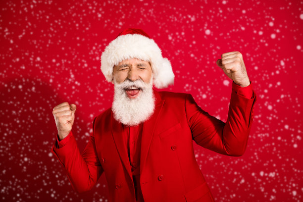 照片万岁白发老人双手拳头戴圣诞帽红色衣服孤立在红色的背景图片下载