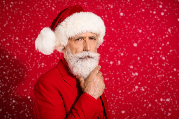 照片严肃的白发老人手胡子戴圣诞帽红色的衣服孤立的红色背景图片下载
